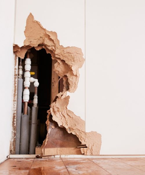 Damaged wall exposing burst water pipes after flood