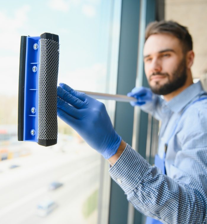 Male janitor cleaning window in office