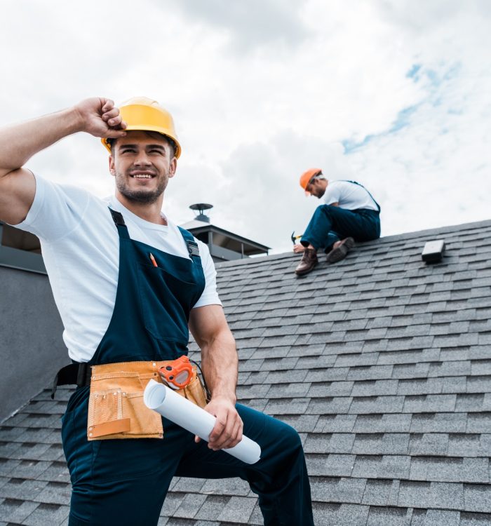selective-focus-of-happy-repairman-holding-rolled-paper-while-coworker-repairing-roof.jpg